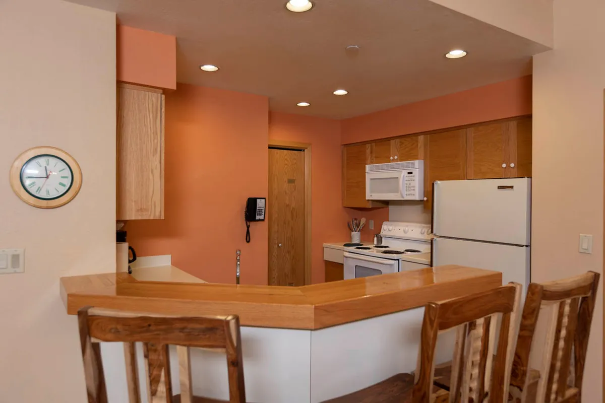 This image showcases a cozy kitchen bar with wooden chairs arranged around it. The modern appliances and ample counter space are visible, along with subtle details suggesting a welcoming environment for cooking, entertaining, and casual dining. The layout encourages gathering and conversation, with plenty of room to prepare and share meals.