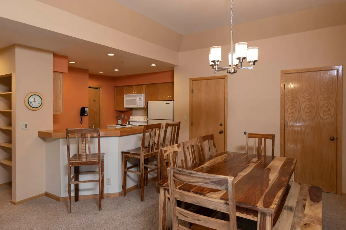 The image features a warm, inviting dining area with a sturdy wooden table surrounded by matching chairs, set beneath a charming chandelier. The nearby kitchen island offers a perfect spot for cooking and socializing, highlighting the open-concept design ideal for gathering. The atmosphere suggests comfort and togetherness, making it easy to envision memorable meals and cozy evenings with loved ones.