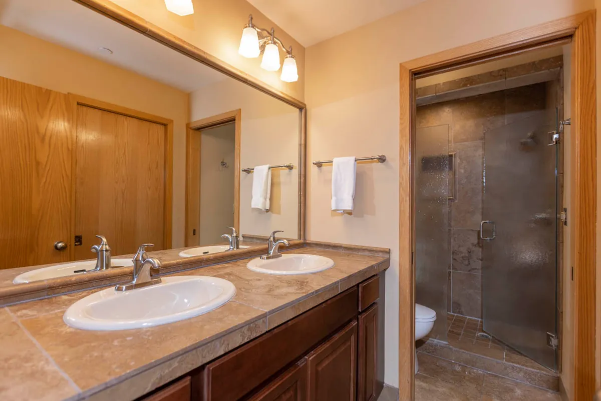A modern bathroom with double sinks, a large mirror, a shower area, and wooden cabinetry, all designed for functionality and style. The space is tranquil, organized, and perfect for self-care routines.