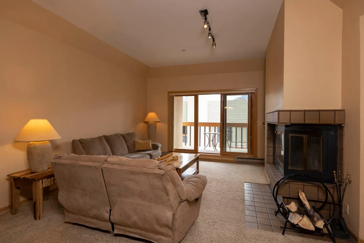 The image offers another angle of the living room, focusing on the sofa, fireplace, and a large window. The composition highlights the open, welcoming layout and the inviting atmosphere ideal for intimate gatherings or quiet moments after a day on the mountain.