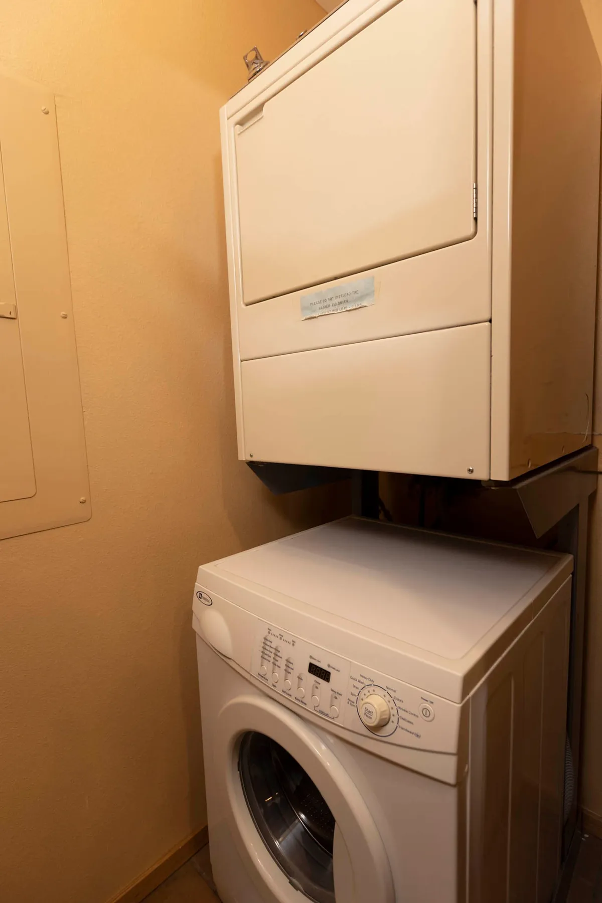 This image features a practical interior space with a stacked washer and dryer alongside a wall-mounted storage panel. The setting suggests a convenient, functional amenity for guests to use during their stay, supporting hassle-free vacation living with organized household tasks.