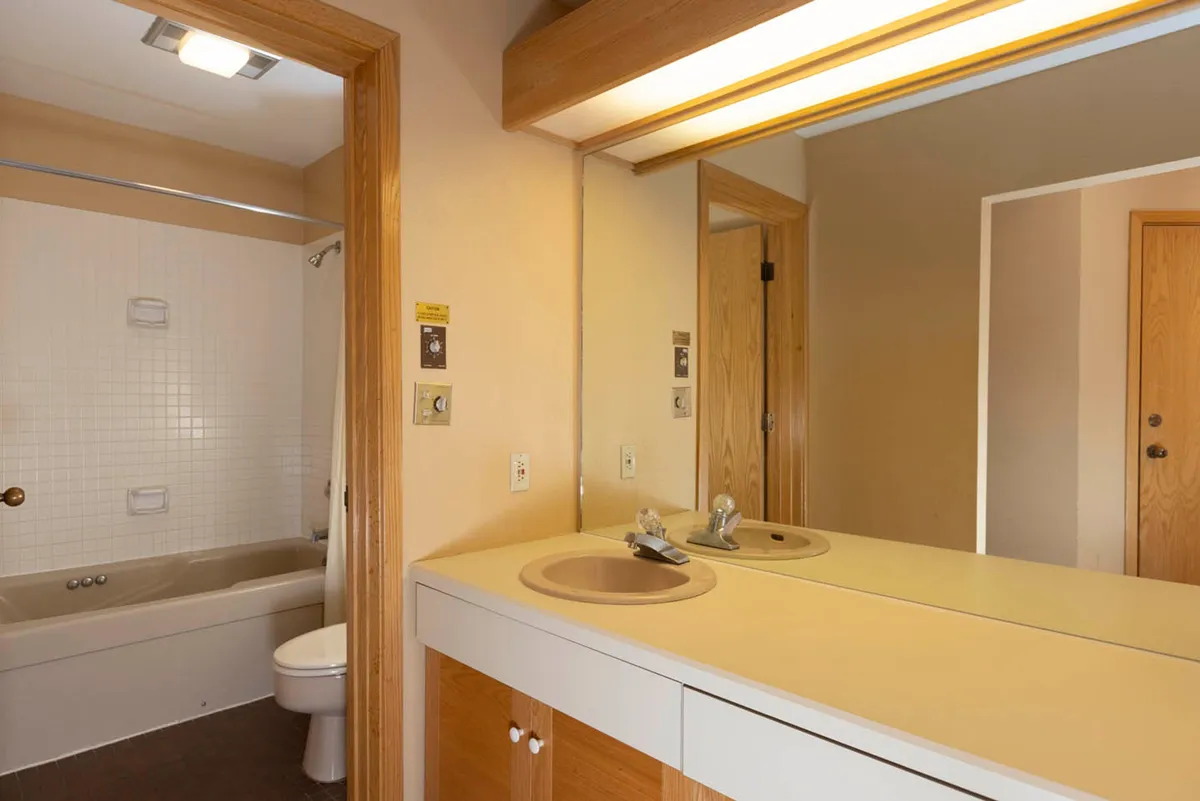 A bright bathroom interior with a double sink, large mirror, shower area, and toilet. Morning light reflects softly in the space, conveying comfort and the ability to refresh after a day outside.